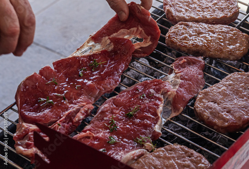 Juicy raw steaks seasoned with herbs and burger patties sizzling on a charcoal grill, captured during a backyard barbecue. Perfect for culinary visuals, grilling ads, or recipe illustrations