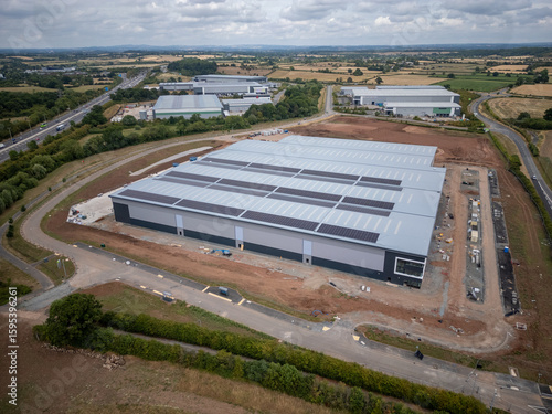 Drone View of Large Sustainable Warehouse Construction Site with Rooftop Solar Panels in Rural UK Business Park – Renewable Energy Industrial Logistics Hub Near Motorway and Countryside