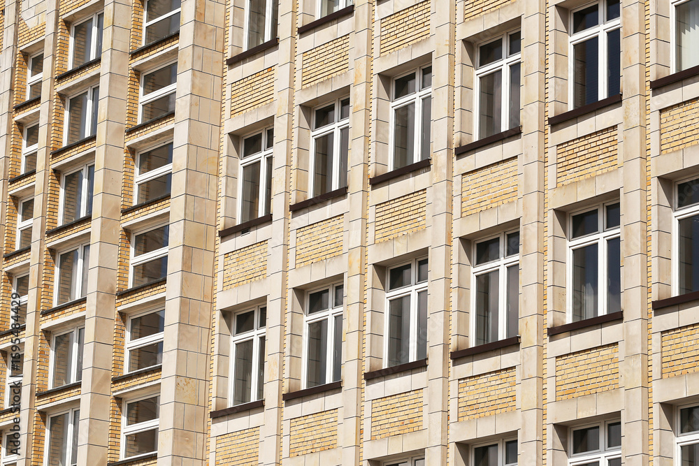 Obraz premium Facade of apartment building. Rows of windows yellow brick wall. Urban architecture with repeating structure. Modern residential exterior. Geometric design in daylight. Vertical residential symmetry.