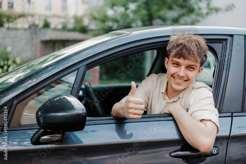 Smiling young man driver showing thumbs up and smiling at camera in car.