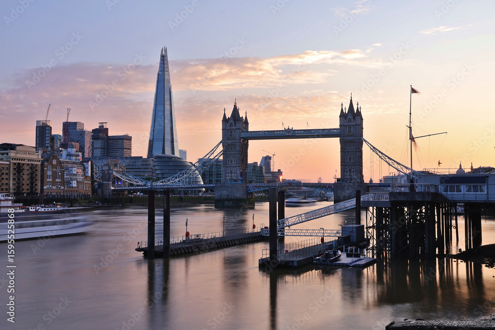 Naklejka premium Sunset long exposure at golden hour of Tower Bridge, London with The Shard and Butlers Wharf; motion-blurred boat on Thames River, docks, gentle pastel pink orange purple sky looking west