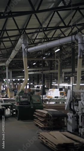 Woodworking machines in industrial workshop. Vertical video inside a modern woodworking factory featuring large industrial machines and an overhead dust extraction system. 
