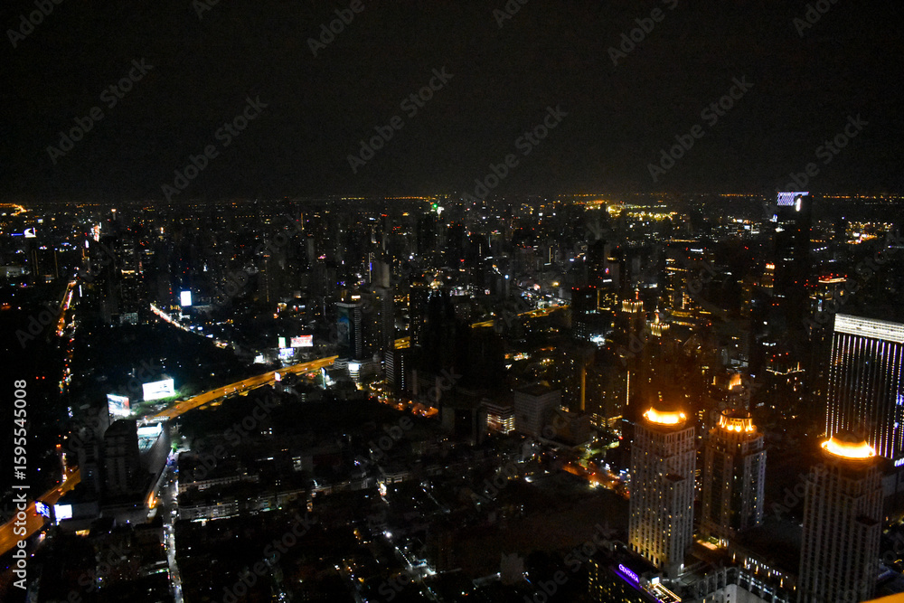 Fototapeta premium An ethereal nocturnal city panorama, adorned with twinkling lights from towering buildings and blurred highways, under a dark sky in Bangkok, Thailand. 