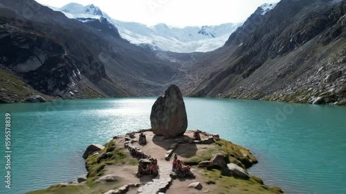 A sacred pilgrimage site with colorful prayer flags and offerings sits on a rocky peninsula in a stunning turquoise glacial lake, with majestic snowcapped mountains in the background