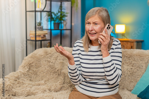 Fotografie Caucasian mature woman sits on home sofa, arguing on phone, showing irritation