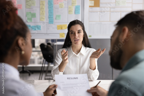 Hispanic female job seeker answering questions about education, skills and knowledge during interview, sitting at table in front of two multiethnic HR manager or head-hunters. Human resources, hiring