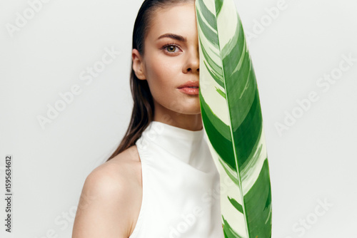 Foto Young woman holding a large green leaf, showcasing a natural and serene beauty in a minimalistic white outfit against a soft background