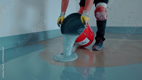 Worker pours light blue self-leveling epoxy resin from a red bucket onto a concrete floor