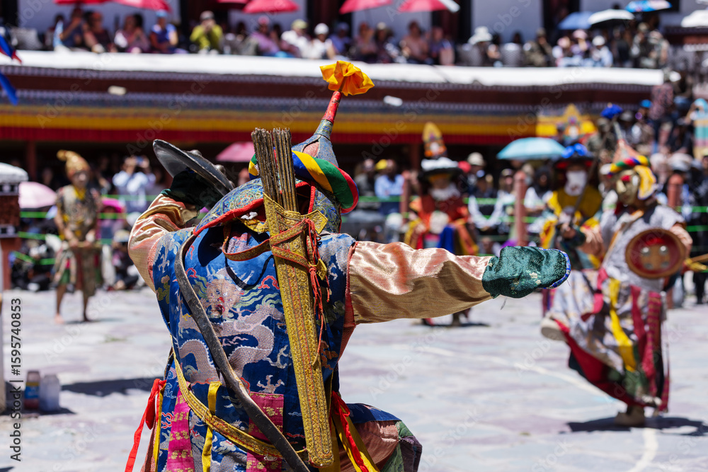 Naklejka premium A masked performer in vibrant costume wields a sword and shield during a dramatic Cham dance at the Hemis Festival in Ladakh. This ritual showcases Tibetan Buddhist culture and ceremonial artistry.