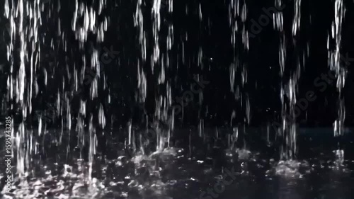 Close-up VFX of heavy rain wall falling in front of the camera against a black screen. Raindrops splash and hit the surface intensely. Practical, seamlessly loopable footage of a powerful rainstorm. I