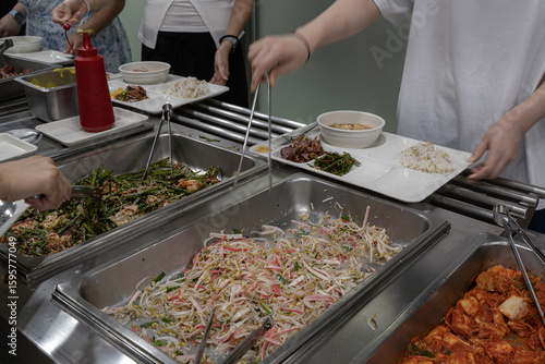 구내식당에서 식판에 한식 반찬을 담는 사람들
