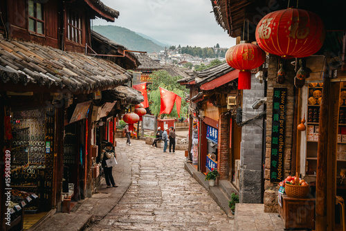 Tourists walk through narrow alley of Lijiang Old Town, China, with traditional tiled roofs