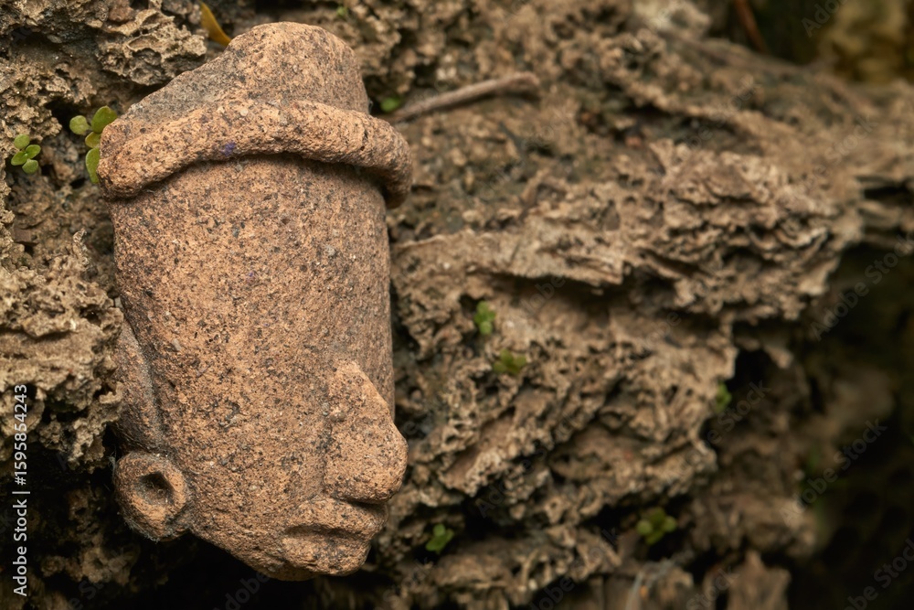 Fototapeta premium A close-up view of an ancient carved clay head partially buried in natural earthy surroundings, evoking archaeological and cultural heritage themes.