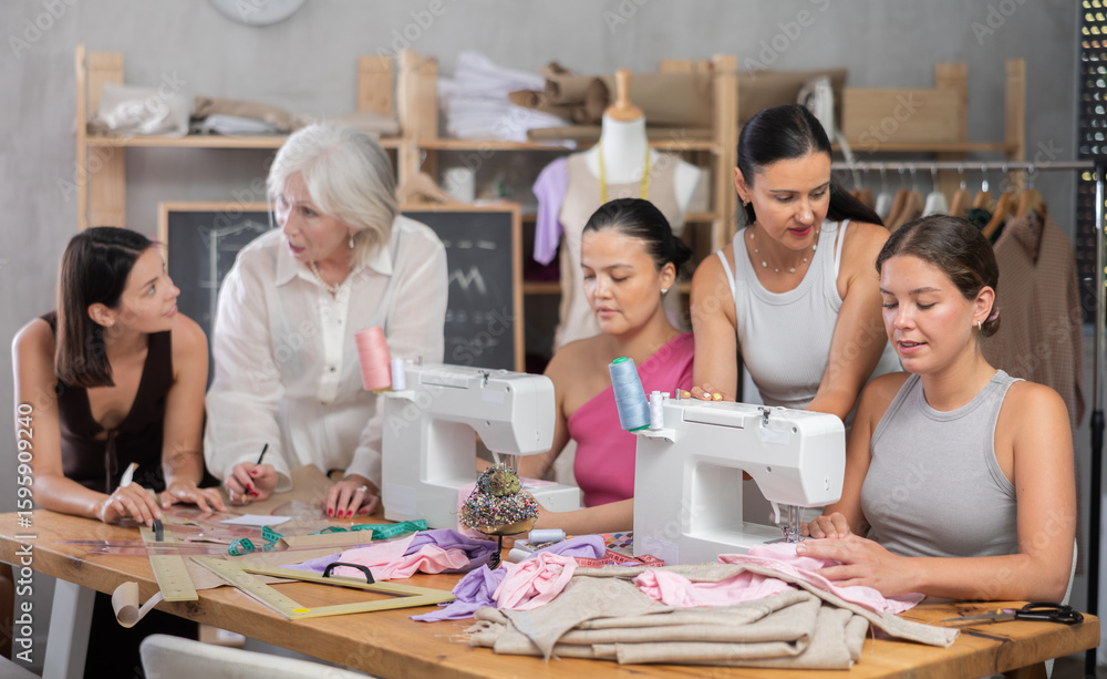 Obraz premium Group of women sewing on machine and draw pattern on paper during lesson at sewing workshop