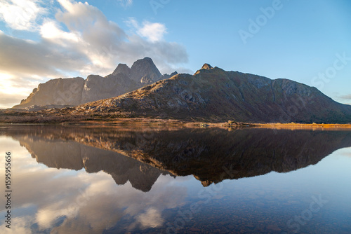 Mountain peaks reflected on a calm lake at sunrise in Lofoten Islands, Norway. Captured with landscape photography techniques using a wide-angle lens and natural golden hour lighting