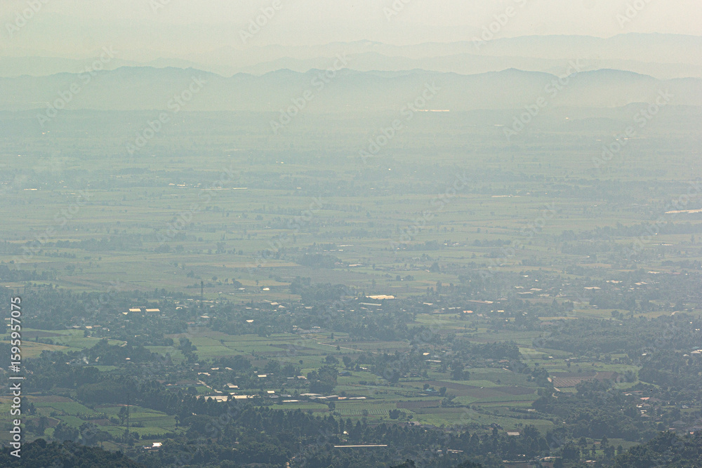 Obraz premium Aerial view of vast green landscape with distant hazy mountains, peaceful rural scenery and natural countryside atmosphere.