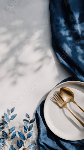 Minimal festive table setting with white plate and golden cutlery on blue silk fabric ideal for christmas dinner designs, seasonal styling and elegant holiday presentations