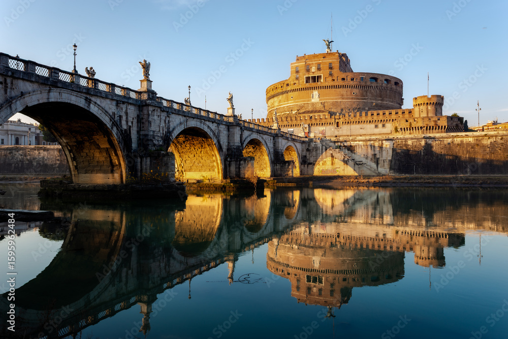 Obraz premium Castel Sant'Angelo and Ponte Sant'Angelo in Rome, Italy, beautifully reflected on the calm surface of the Tiber River during golden hour. This landscape photograph captures the historical architecture