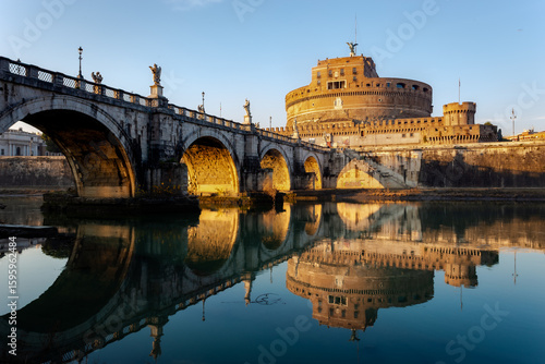 Castel Sant'Angelo and Ponte Sant'Angelo in Rome, Italy, beautifully reflected on the calm surface of the Tiber River during golden hour. This landscape photograph captures the historical architecture