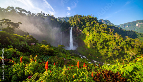 Tall waterfall flowing heavily with surrounding mist, surrounded by tropical green trees.