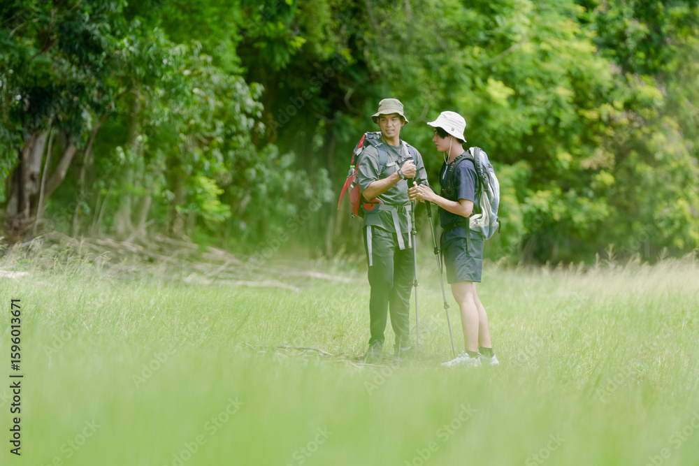 Fototapeta premium Happy tourist hiking walking together over grassland of the plains. Active young adult man trekking through nature grass field over lowland in rural trail. Portrait of real people in peaceful meadow.