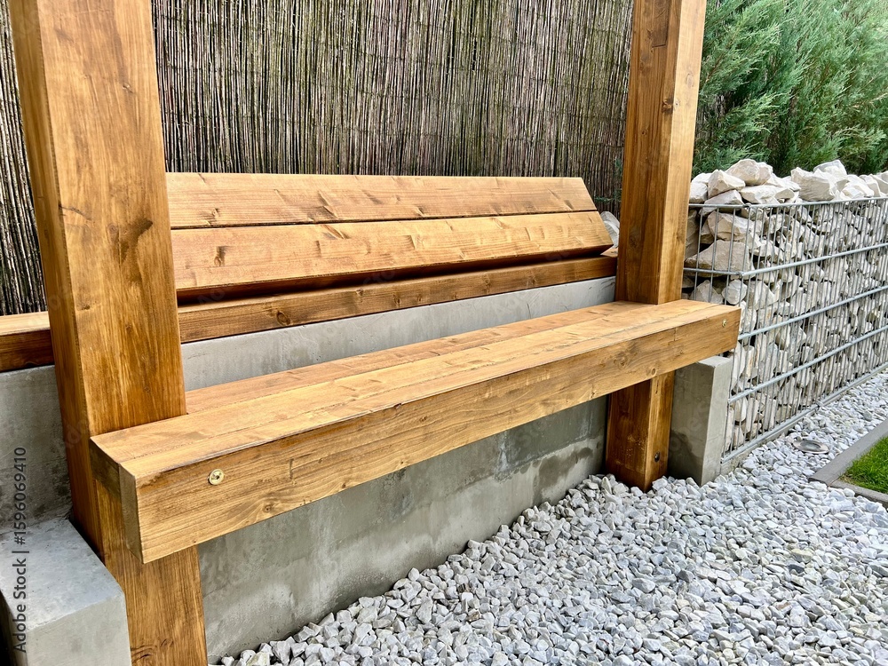 Fototapeta premium A simple yet inviting scene featuring a wooden bench placed in a contemporary urban garden, surrounded by greenery and modern landscaping. Perfect for themes of relaxation, city life, and green urban 