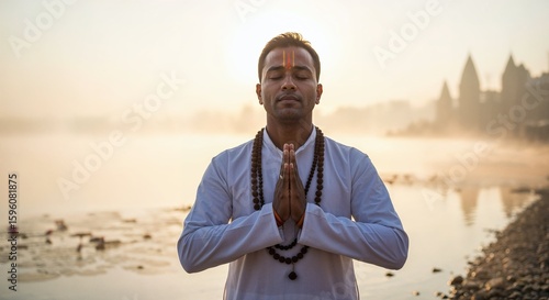 Man in white shirt meditating by river at sunrise with hands together