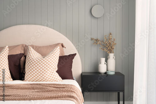 Close up shot of cushions in cotton pillowcases on comfortable bed near side table with flower vase in cozy bedroom at home. Grey timber patterned back ground wall with natural light shears.