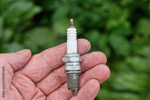 Fototapeta Naklejka Na Ścianę i Meble -  one small metal white gray spark plug lies on the open palm of the hand on a green background on a summer street