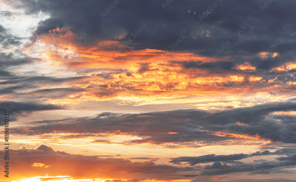 Fototapeta premium Dramatic evening sky with glowing orange clouds illuminated by the setting sun against a dark and moody background.