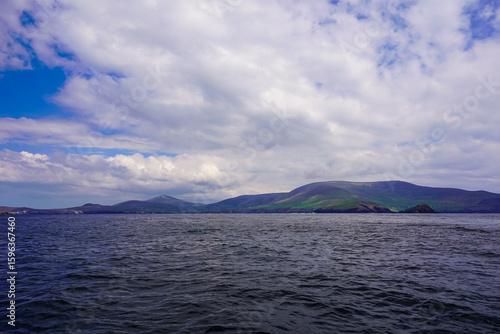Distant view of green hills and cloudy sky above dark ocean water.