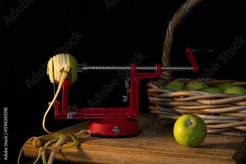 Canvas Print A red apple corer sits on a wooden table next to a basket of apples