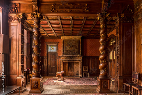 Ornate abandoned mansion interior with carved wooden columns, vintage fireplace, antique rocking horse and classic furniture in warm natural light