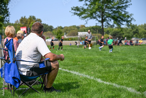 Parents enjoy a sunny day at a youth soccer match while supporting their kids on the field