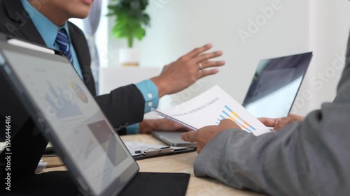 Business professional analyzing data in graph document and sharing insights during meeting with partners. Manager identifying trends, business challenges.