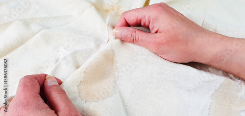 A woman is holding a white cloth with a stain on it. Dirty, stained cloth, thing, washing, dry cleaning.