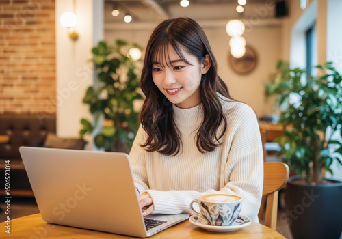 カフェで、笑顔で楽しくパソコン作業をする白いセーターを着た女性