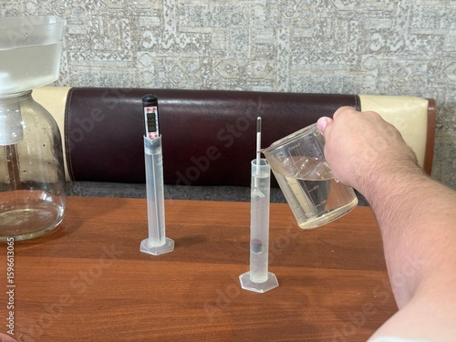 Fotografi Close up hand of man carefully pouring liquid into graduated cylinder next to di