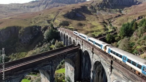 Aerial view of a train crossing a stone viaduct in a mountainous landscape area