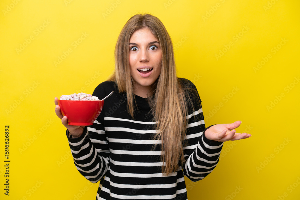 Young caucasian woman holding a bowl of cereals isolated on yellow background with shocked facial expression Young caucasian woman holding a bowl of cereals isolated on yellow background with shocked facial expression