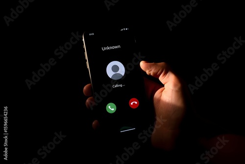 Hand holding mobile phone with unknown caller notification, concept of telephone fraud, call blocking, digital security, unwanted calls, anonymous communication, phishing attempt.