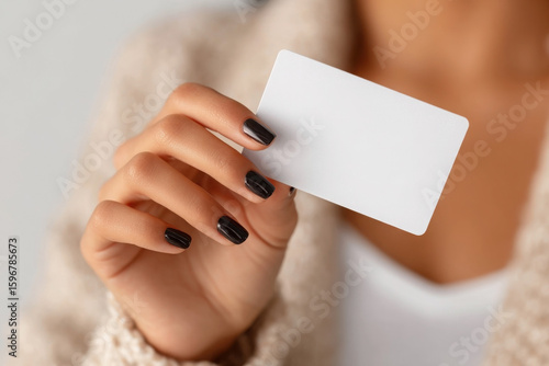 Close-up of a woman's hand with black nails elegantly holding a blank white credit card against a solid white backdrop. mockup credit card, bank card, gift certificate