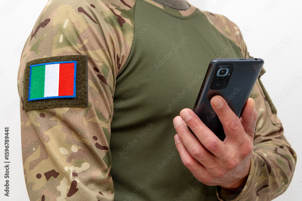 Fototapeta premium A man in military uniform with Italian flag patch holding a mobile phone.
