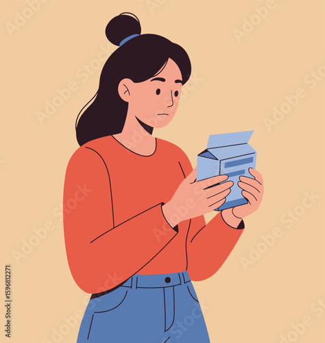 Confused young woman with a dark hair bun in a red sweater reading a product box.
