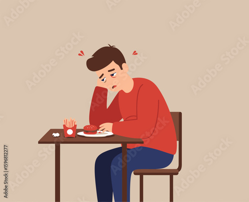Tired young man with red eyes and a sad expression sitting at a table with a fast food meal of a burger and fries.