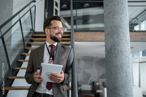 Tableau sur toile Smiling businessman holding tablet and looking away in modern office building