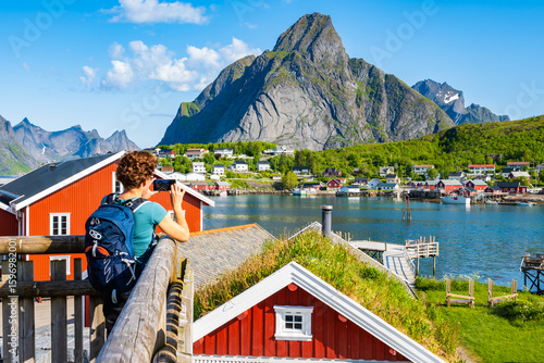 Female hiker taking picture of spectacular view of Reine village with sea and mountains, Lofoten Islands, Norway