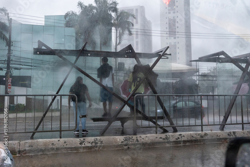 People are seen through a glass window with raindrops taking shelter from the rain at a bus stop during a storm in Sao Paulo, Brazil.