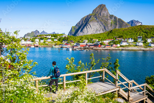 Female hiker enjoying spectacular view of Reine village with sea and mountain...