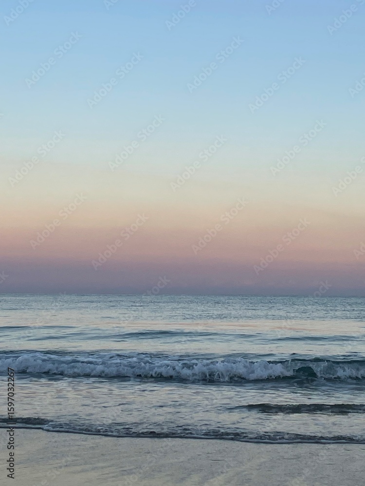 Fototapeta premium sunset over the sea with small waves crashing in the water without a cloud in the sky